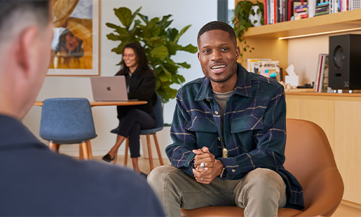 Justin sitzt in einem Bürogebäude in einer Lounge und unterhält sich mit einem Apple Teammitglied.