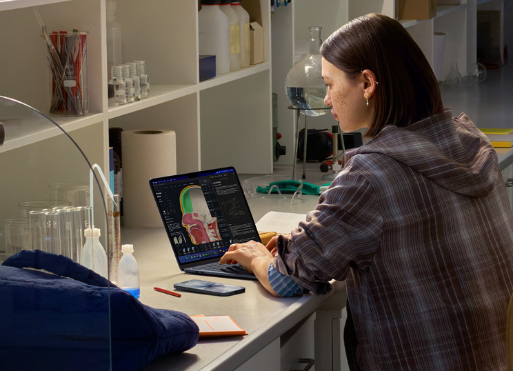 Una persona seduta in un laboratorio che usa un MacBook, il cui schermo mostra diverse app.