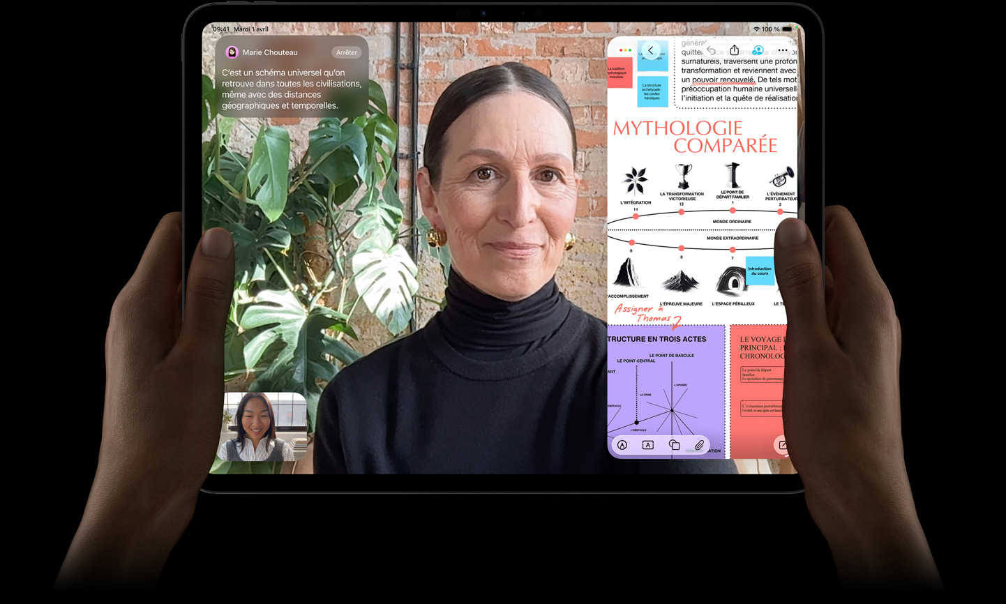 iPad Pro, face avant, noir sidéral, mains gauche et droite tenant l’appareil en orientation paysage, angles arrondis, cadre d’écran noir, écran affichant une conversation FaceTime traduite en direct et une app éducative montrant une présentation de la mythologie comparée avec du texte, des diagrammes et des notes manuscrites