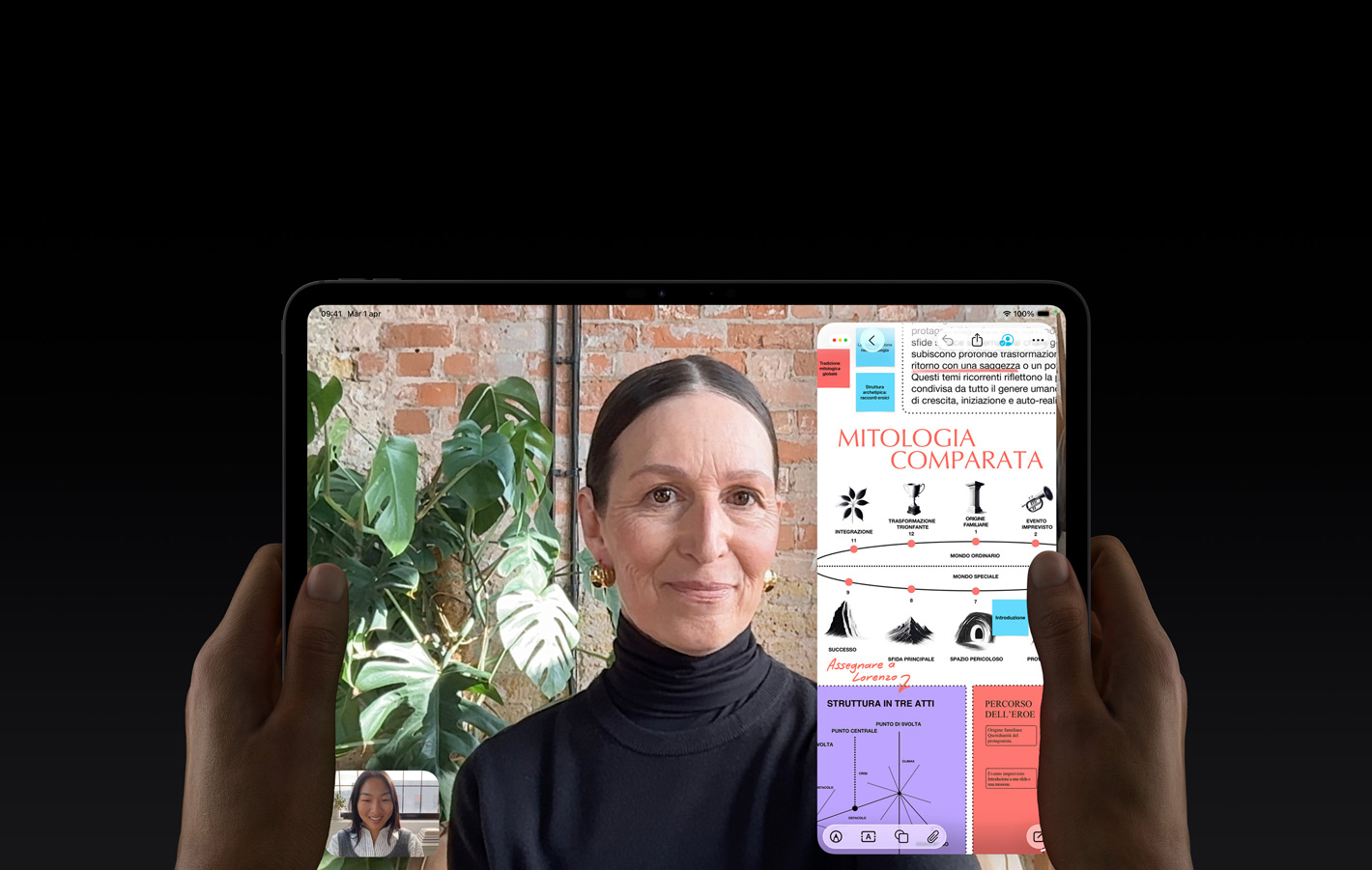 Un iPad Pro nero siderale, mostrato di fronte, tenuto fra due mani in orizzontale, angoli arrotondati, cornice del display nera, display che mostra una conversazione FaceTime con traduzione automatica in tempo reale, e un’app didattica con una presentazione sulla mitologia comparata con testo, diagrammi e note scritte a mano