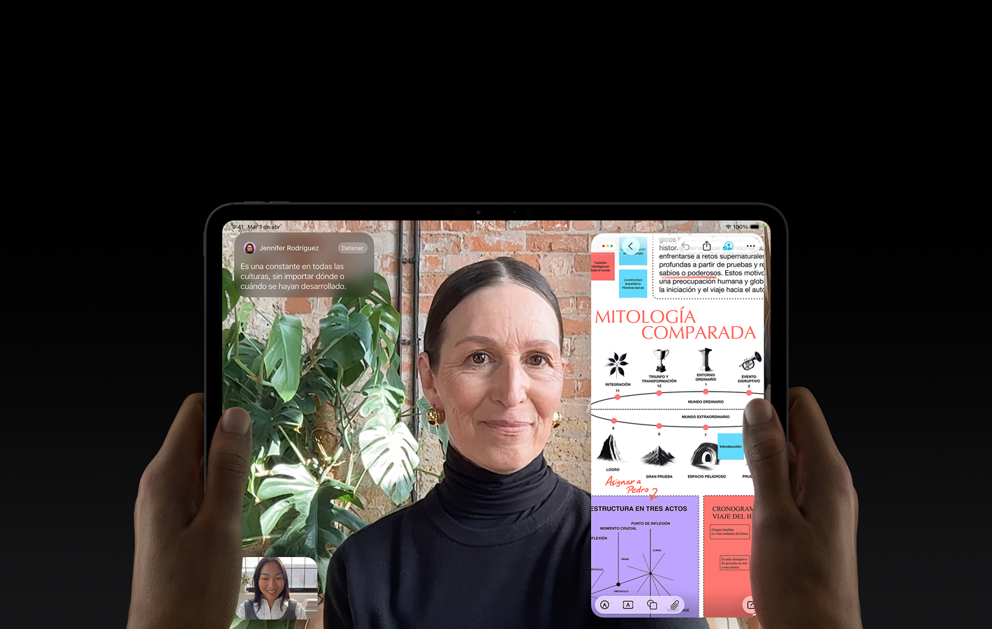 iPad Pro, parte frontal, color negro espacial, manos izquierda y derecha lo sostienen en posición horizontal, esquinas redondeadas, marco de la pantalla negro, la pantalla muestra una conversación en FaceTime que se está traduciendo en vivo, y una app educativa con una presentación sobre mitología comparada con texto, diagramas y notas escritas a mano