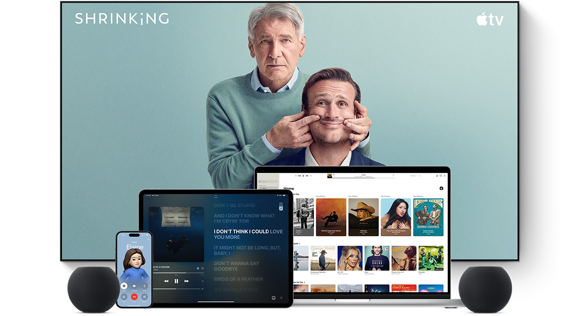 Large flat-screen television showing two male characters from the Apple TV series Shrinking. A MacBook Pro, an iPad, an iPhone and a Midnight HomePod mini are arranged in front.
