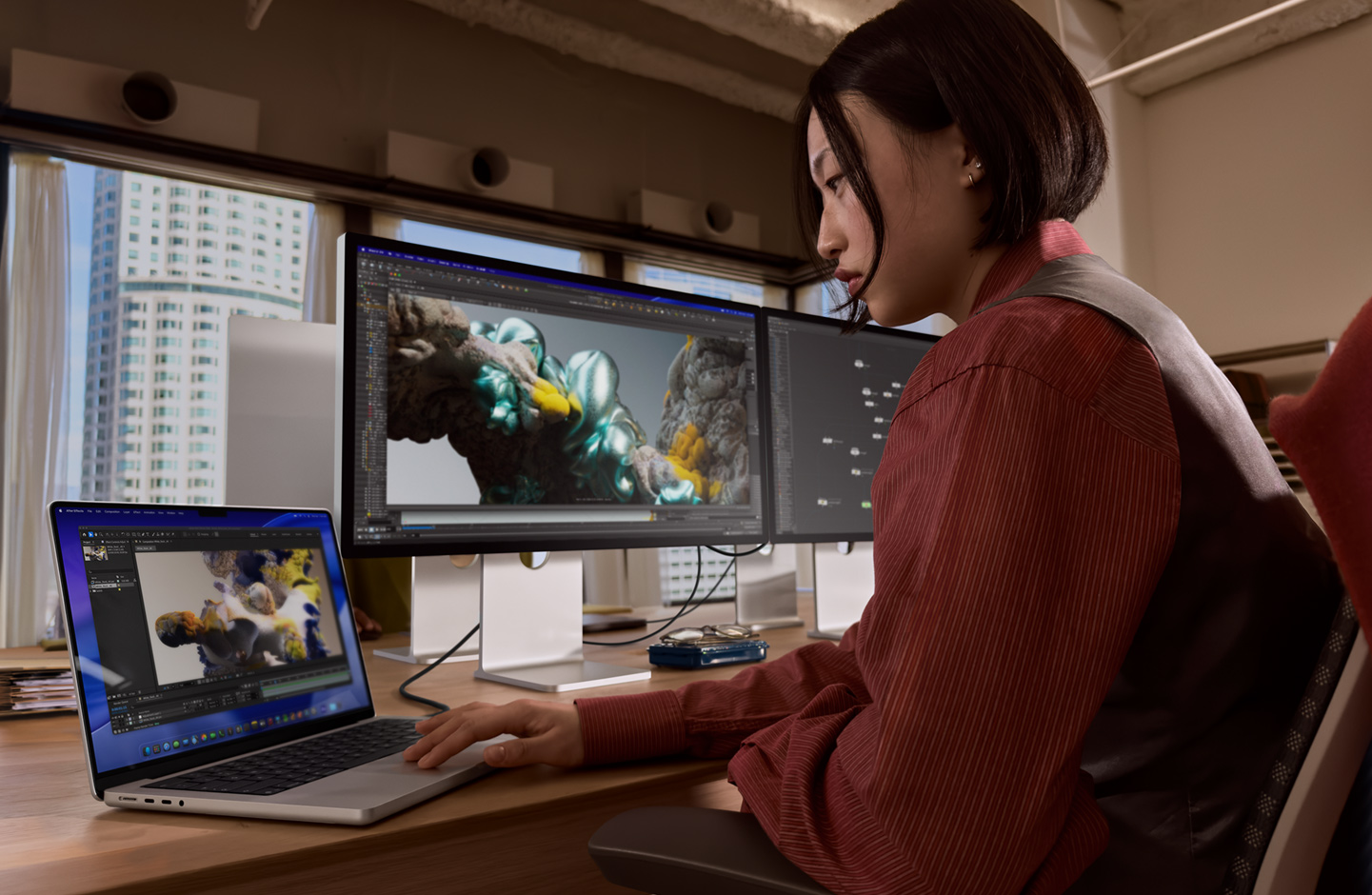 Osoba v kancelárii pracuje na MacBooku, ku ktorému je cez port Thunderbolt 5 pripojený Studio Display XDR