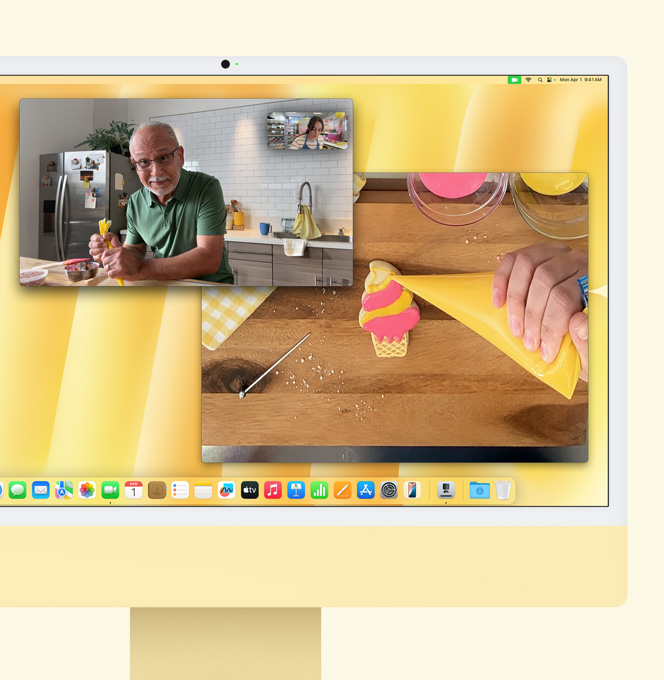 黃色 iMac。桌面視角功能示範。畫面展示烘焙師在與另一個人進行視訊通話。一個畫面顯示烘焙師與男士的臉部。另一個畫面顯示烘焙師動手為餅乾加上糖霜