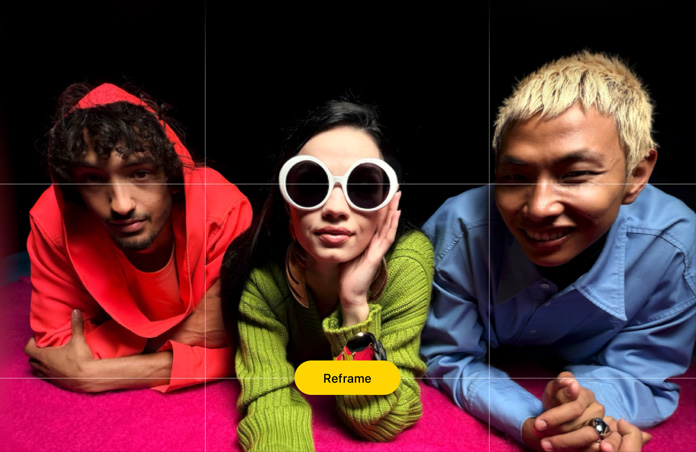 Brightly hued closeup photo of three people leaning forward over a pink surface, a grid appears over it, along with a button that reads: Reframe