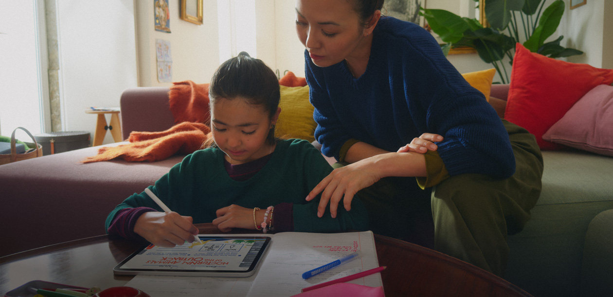 A child using an iPad to draw in the living room while an adult supervises from the sofa.