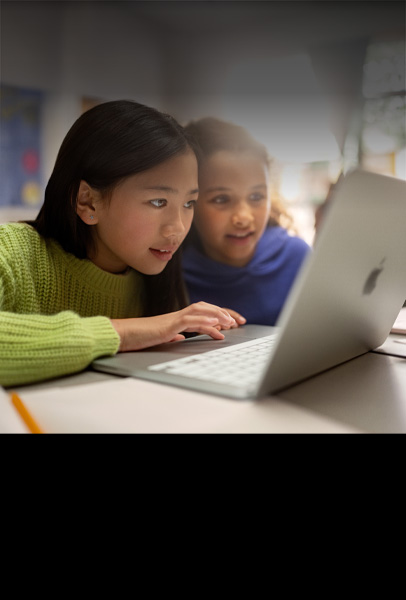 兩位年幼學生坐在教室的書桌前，全神貫注，使用 MacBook 進行協作