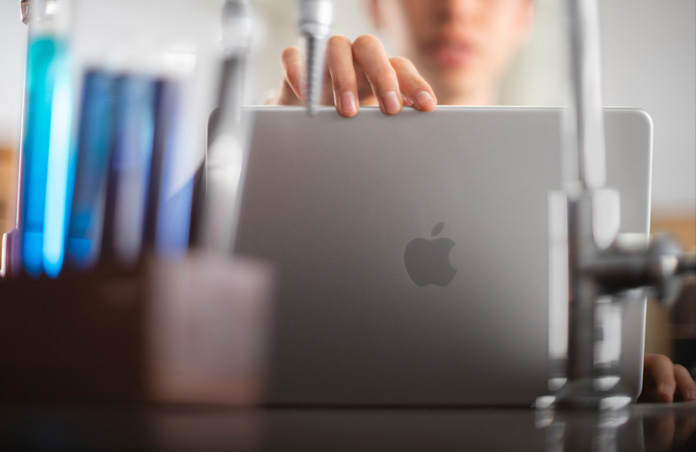 Student rests hand on thin bezel of open MacBook in lab environment