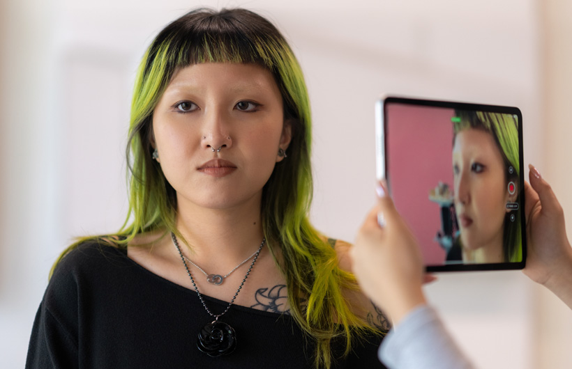 A student with green-tinted hair gets her face scanned with an iPad camera.