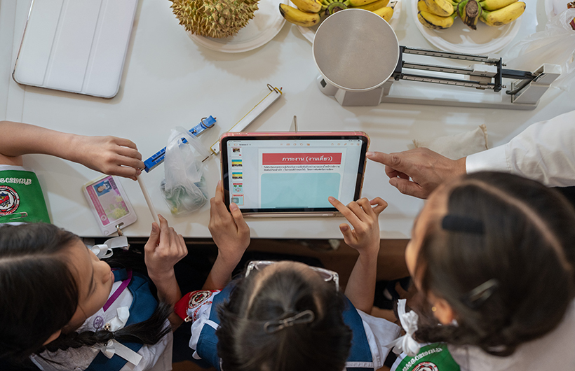 Drei Grundschüler:innen arbeiten gemeinsam mit einem iPad an einer Präsentation für ein naturwissenschaftliches Projekt.