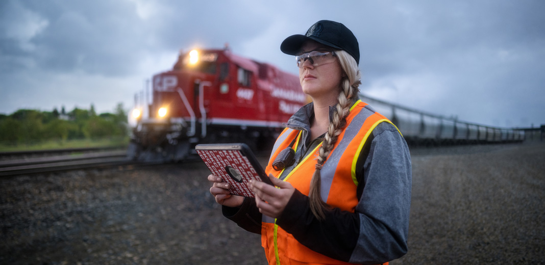 A railway worker holds an iPad and looks out at the tracks as a train passes by