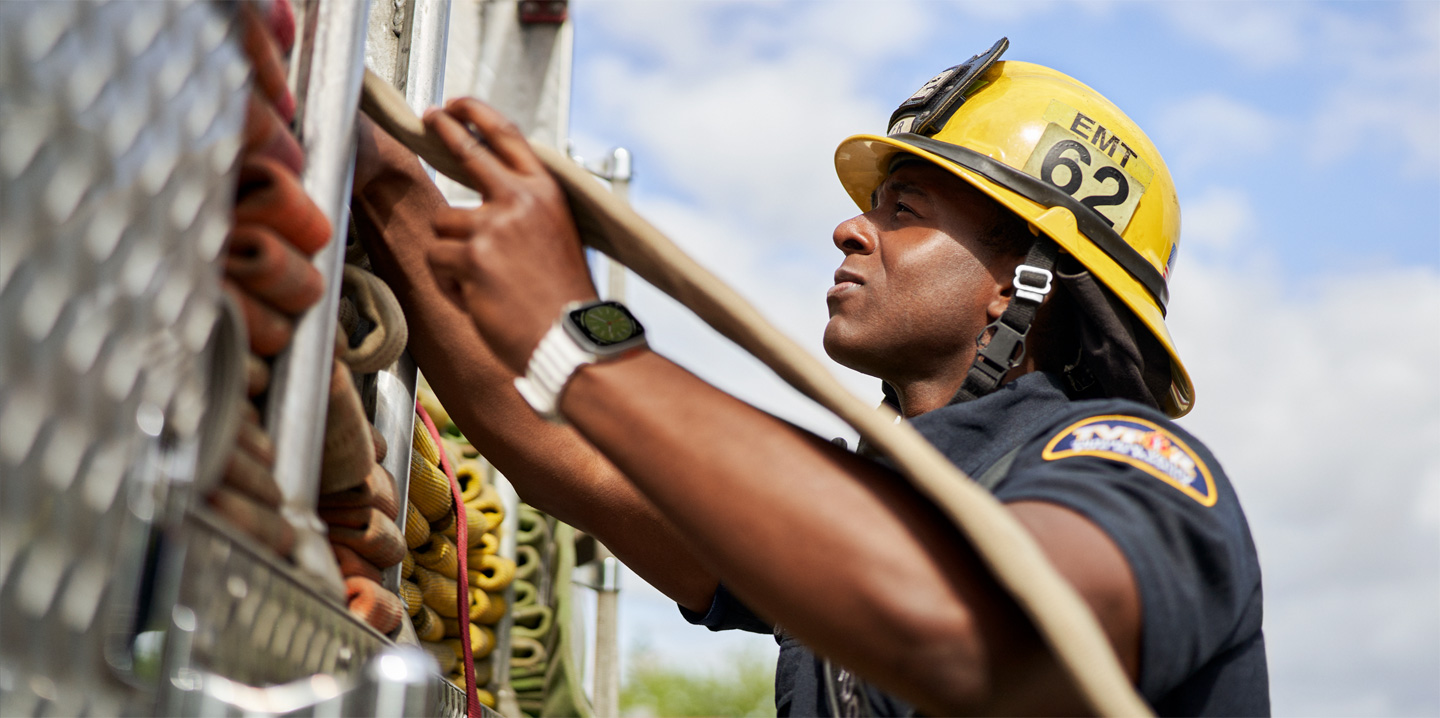 A firefighter pulls a hose out of a fire engine while wearing an Apple Watch