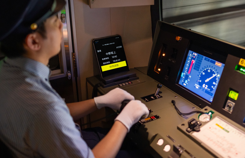 Ein iPad mit Stationen und Zeiten auf dem Display steht neben dem Steuerpult, an dem ein Zugführer arbeitet.