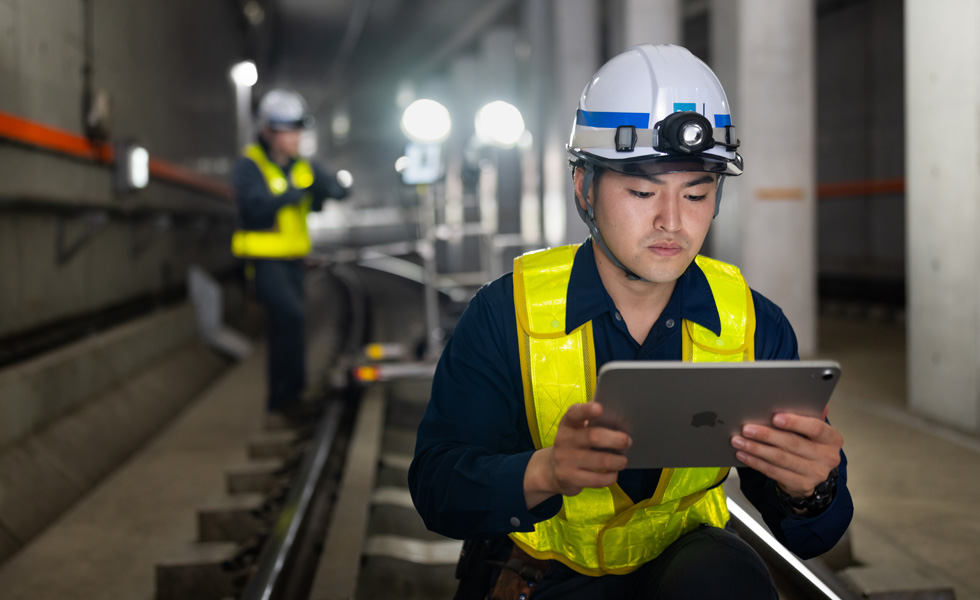 Ein Arbeiter, der eine Sicherheitsweste und einen Schutzhelm trägt, blickt auf ein iPad, während er Wartungsarbeiten in den Tunneln der Tokyo Metro durchführt.