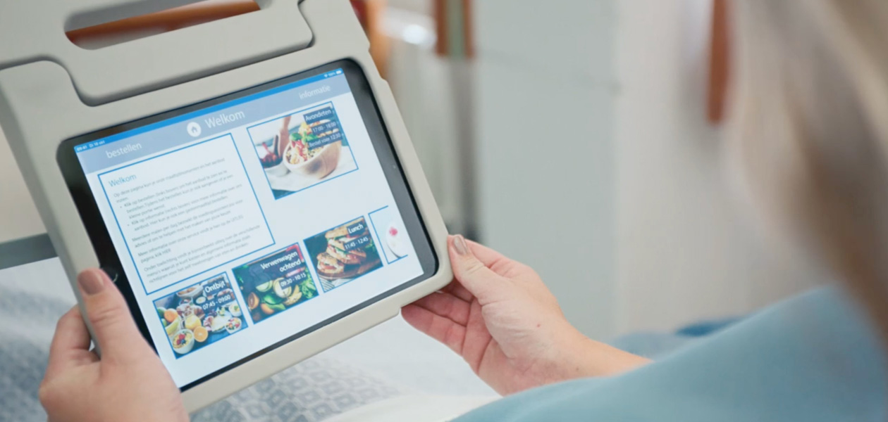 Een patiënt kijkt in haar ziekenhuisbed naar een iPad-scherm.
