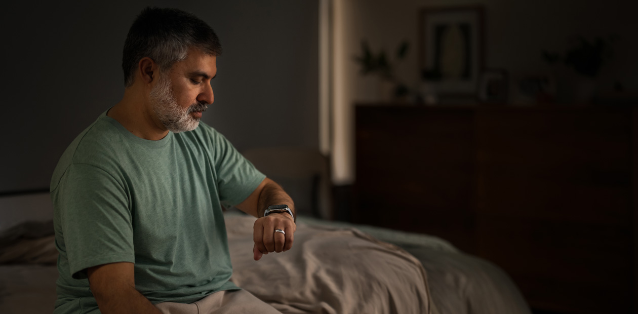 Een man zit in bed en kijkt op zijn Apple Watch.