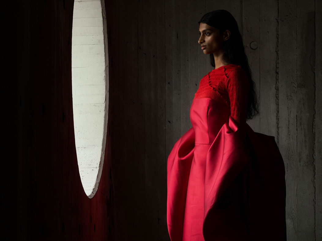 ผู้หญิงใส่ชุดเดรสยาวสีแดงยืนโพสท่าถ่ายภาพอยู่ในห้องว่างๆ แอปรูปภาพสลับเป็นทางยาวโฟกัสช่วงต่างๆ ตั้งแต่ 200 มม. ถึง 13 มม. เพื่อแสดงความสามารถของระบบกล้องระดับโปร