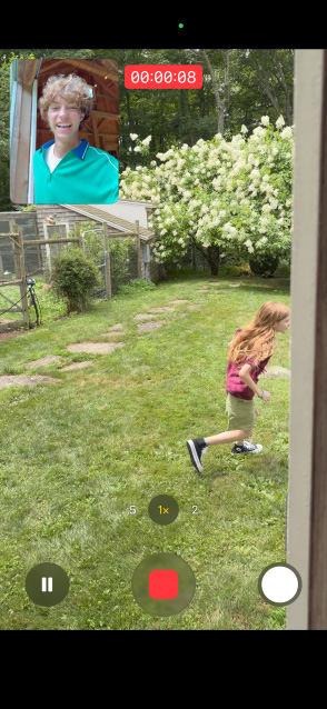 Écran d’un iPhone 17 montrant l’utilisation des caméras avant et arrière pour la vidéo double capture d’une jeune fille qui court pendant qu’un homme la regarde