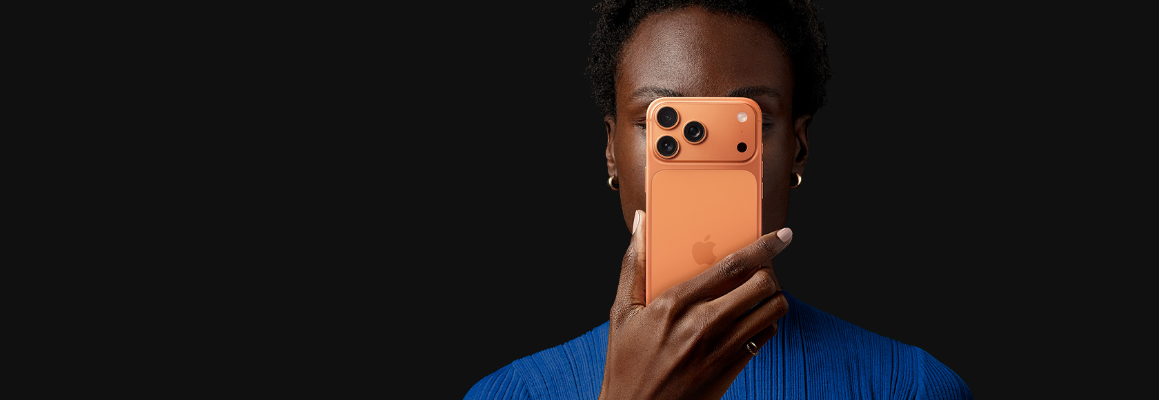 Una persona sostiene un iPhone 17 Pro frente a su cara, con la parte posterior hacia fuera, color naranja cósmico